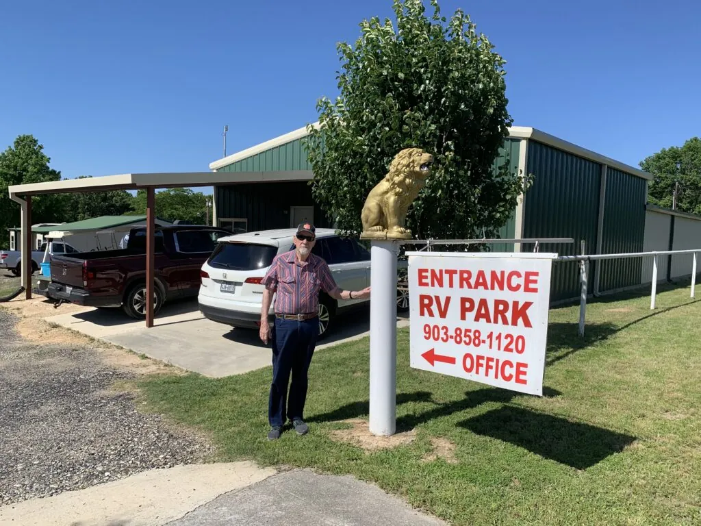 The owner of Lion's RV Park at the park entrance, beside the golden lion and RV Park office sign in Tyler, Texas